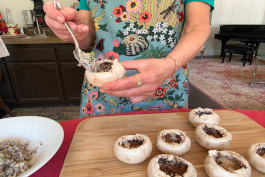 Maria holds a mushroom cap in her hand and fills it with veggie mince with a spoon.