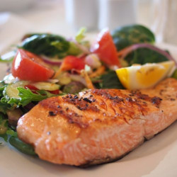 Baked salmon on a plate with herbs, chopped tomatoes, and onion slices