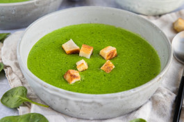 A vibrant green soup garnished with crouton pieces, served in a white bowl.