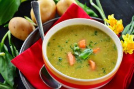 A vibrant green soup garnished with pieces of carrots and pieces of green onion, served in a red bowl.